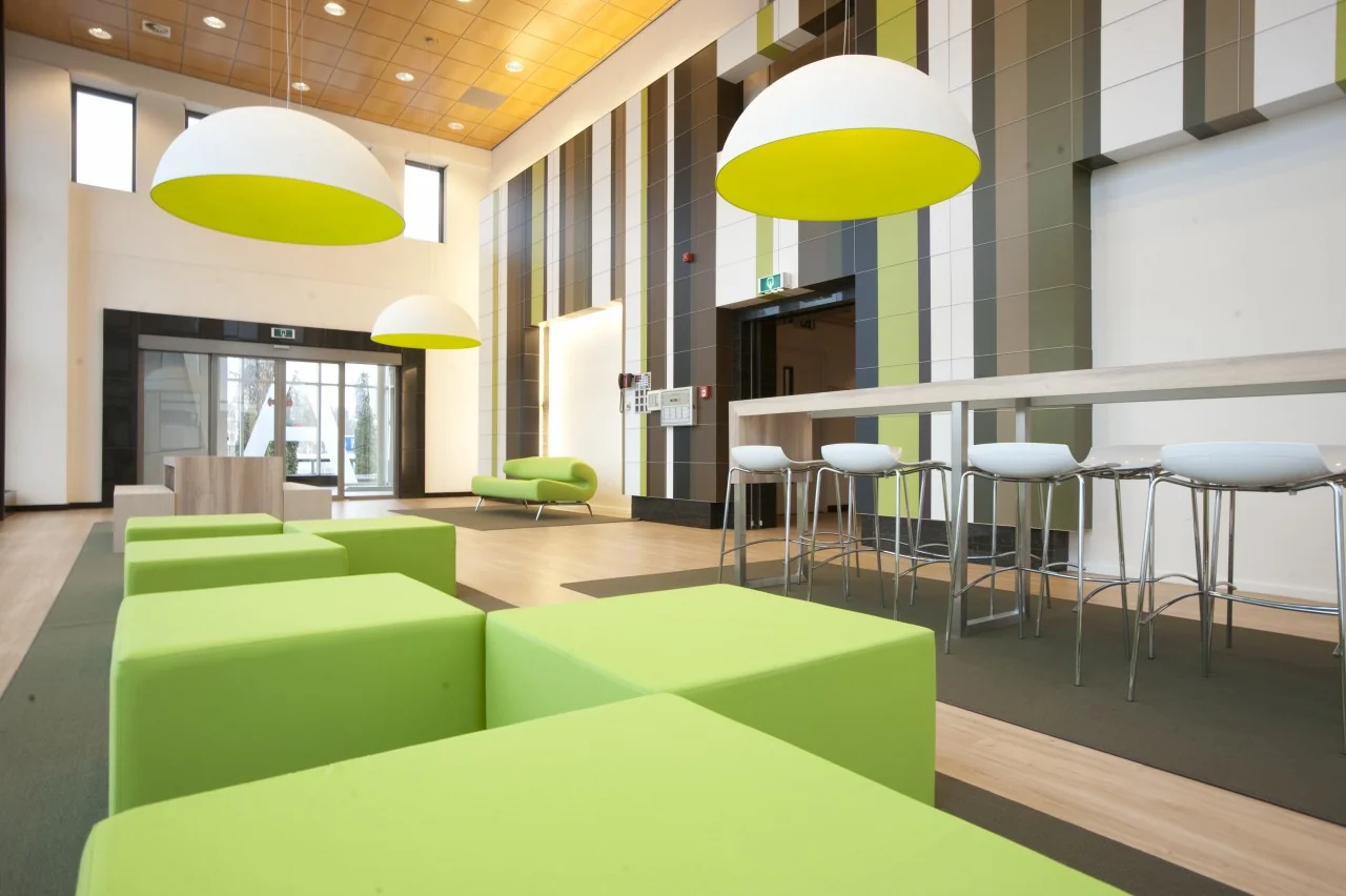 Moderne lobby aan het Rivium Boulevard met felgroen meubilair, hoge krukken en grote hanglampen.